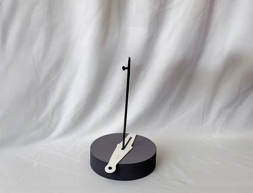 A duck float stand without a duck decoy against a white cloth background.