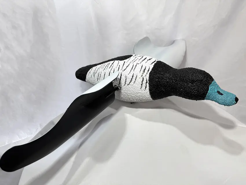 Realistic bluebill duck decoy featuring a textured teal head, black neck, white speckled body, and large curved motion wings, displayed on a white fabric backdrop.